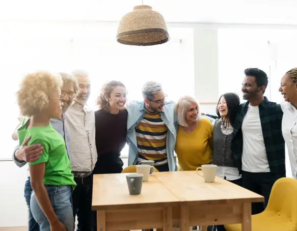 Diverse grupp av bostadsrättsföreningsmedlemmar som umgås och skrattar tillsammans i ett gemensamt kök hos styrelseskolan.